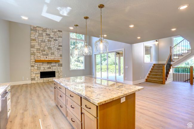 Kitchen with open floor plan, light wood-style floors, light stone counters, a skylight, and a center island | Image 11