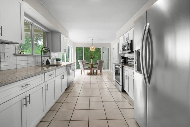 Kitchen with appliances with stainless steel finishes, tasteful backsplash, light tile floors, a sink, and white cabinets | Image 6