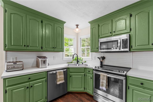 Kitchen with a textured ceiling, a sink, light countertops, appliances with stainless steel finishes, and dark wood-type flooring | Image 16