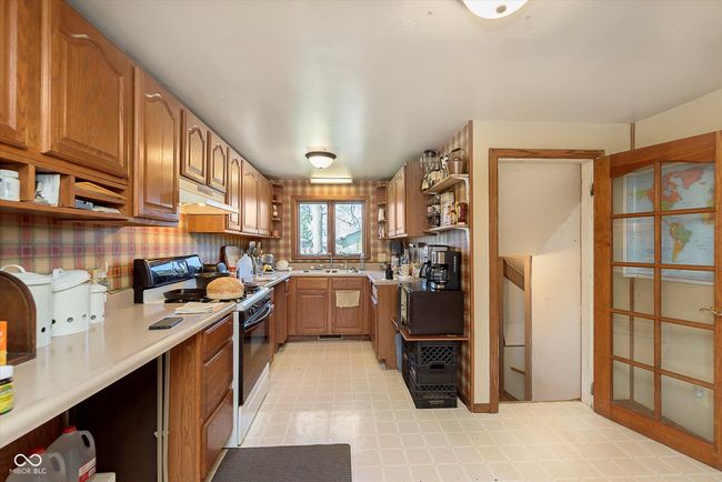 kitchen featuring light countertops, open shelves, under cabinet range hood, range with electric stovetop, and a sink | Image 12