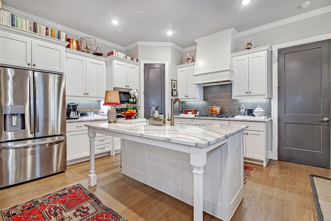 Kitchen with custom exhaust hood, appliances with stainless steel finishes, white cabinetry, and light wood finished floors | Image 11