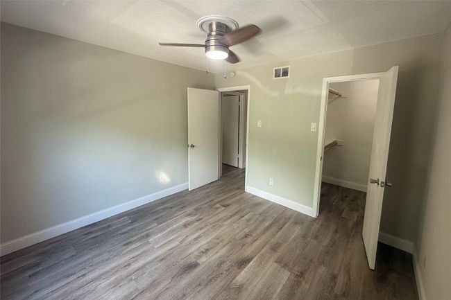 Unfurnished bedroom featuring wood finished floors, a walk in closet, a closet, and a ceiling fan | Image 6