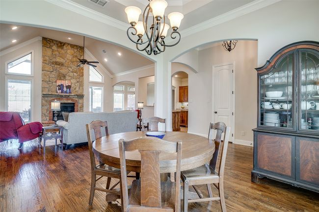 Dining space with visible vents, dark wood-style flooring, ornamental molding, a stone fireplace, and ceiling fan with notable chandelier | Image 6
