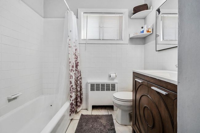 Bathroom featuring toilet, tile walls, radiator, shower / tub combo, and vanity | Image 14