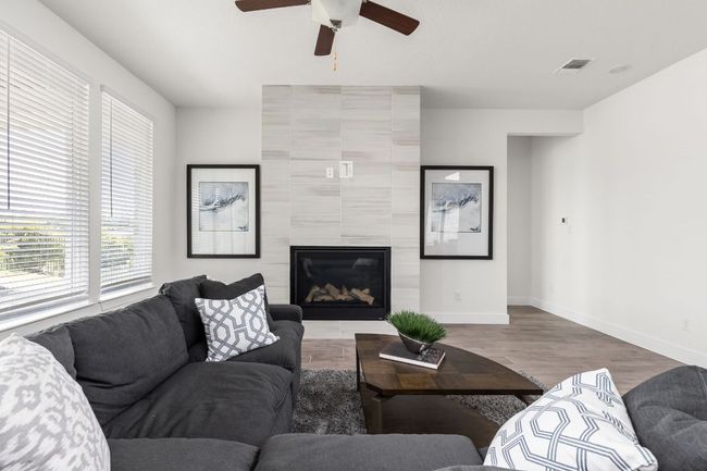 Living room with ceiling fan, a glass covered fireplace, wood finished floors, and baseboards | Image 18