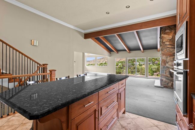 Kitchen with appliances with stainless steel finishes, light colored carpet, light tile patterned floors, dark stone counters, and brown cabinetry | Image 17