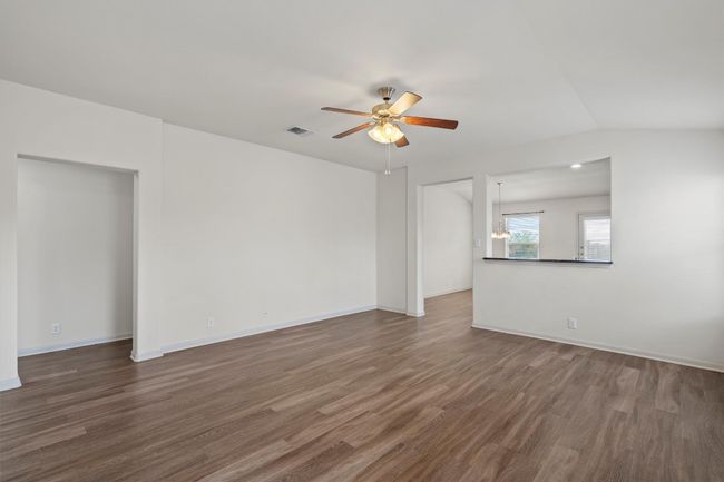 The living room featuring a ceiling fan and the LVP flooring leads you into the kitchen. | Image 4
