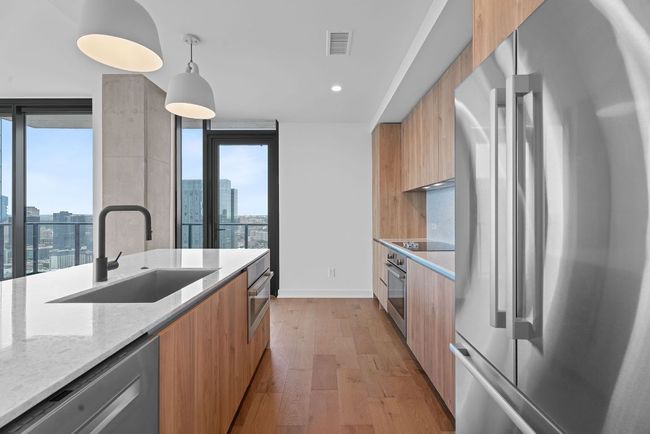 Kitchen with stainless steel appliances, modern cabinets, light wood-style floors, light stone counters, and a city view | Image 6
