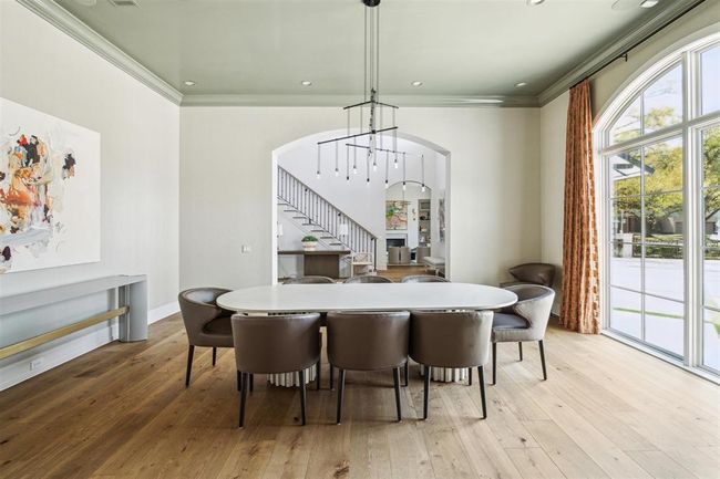 The formal dining room exudes sophistication, framed by a graceful arched cased opening and anchored by an elegant Sonneman Suspenders chandelier. Expansive windows overlook the manicured grounds, filling the space with natural light. It's a stunning, welcoming room that sets the tone as you enter the home. | Image 5