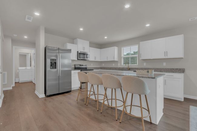 A sleek, contemporary kitchen featuring stainless steel appliances, elegant white cabinetry, granite countertops, and a spacious island perfect for meal prep and casual dining. Refrigerator stays! | Image 16