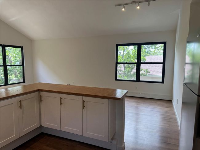 Kitchen featuring butcher block countertops, lofted ceiling, dark wood-style flooring, freestanding refrigerator, and white cabinetry | Image 6