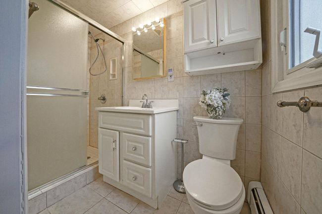 Bathroom featuring tile patterned flooring, tile walls, an enclosed shower, a baseboard radiator, and vanity | Image 23
