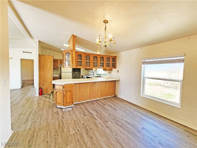 Kitchen with brown cabinets, glass insert cabinets, freestanding refrigerator, light wood finished floors, and a notable chandelier | Image 7
