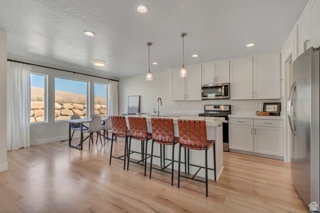 Kitchen with stainless steel appliances, white cabinetry, light wood finished floors, a kitchen bar, and recessed lighting | Image 7