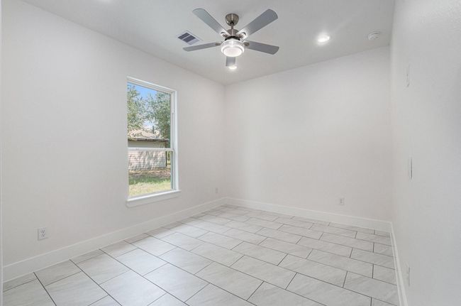 This bright room features large tile flooring, a ceiling fan with lights, and a window providing natural light and a view of the yard. The neutral walls enhance the spacious feel, making it a versatile space for any purpose. | Image 40