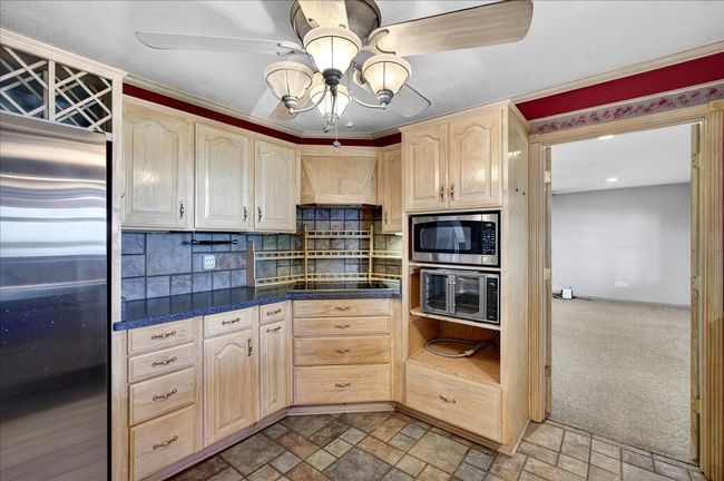 Kitchen with appliances with stainless steel finishes, light brown cabinets, ceiling fan, dark countertops, and backsplash | Image 20