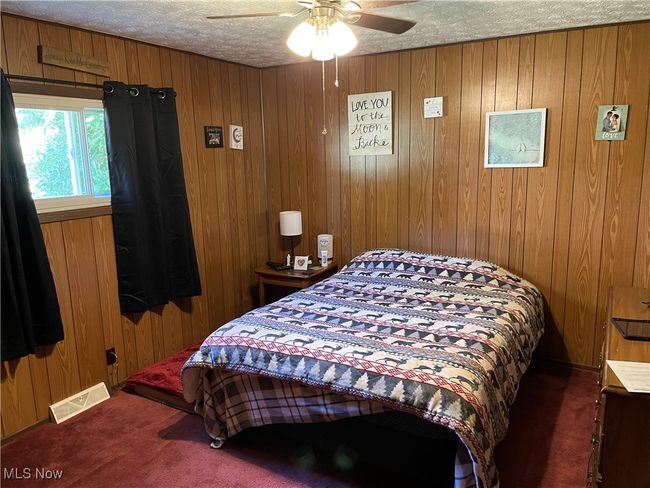 Carpeted bedroom featuring ceiling fan, wood walls, and a textured ceiling | Image 12