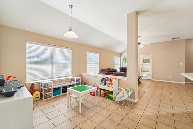 Bright, open living space with tiled floors, featuring a play area and cozy seating. Large windows provide natural light, and there's easy access to the backyard through a glass door. Perfect for family living. | Image 5