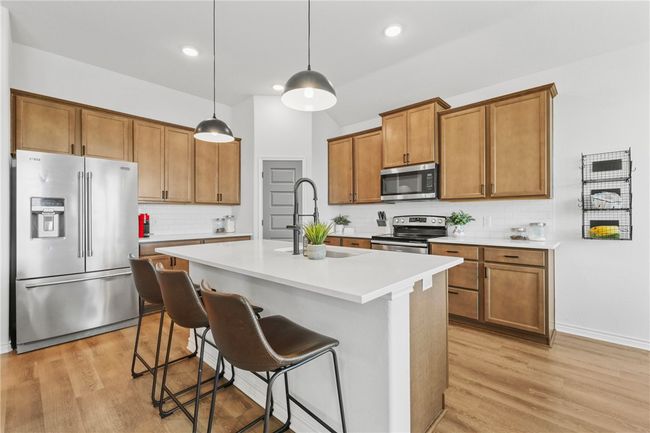 Kitchen featuring stainless steel appliances, brown cabinetry, light wood finished floors, backsplash, and recessed lighting | Image 14