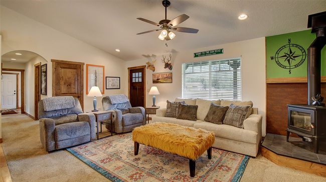 Carpeted living area featuring a wood stove, ceiling fan, arched walkways, vaulted ceiling, and recessed lighting | Image 5