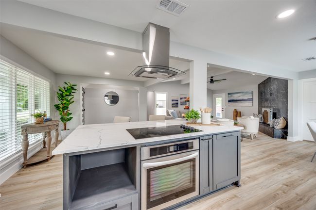 Kitchen featuring oven, black electric stovetop, open floor plan, island exhaust hood, and light stone counters | Image 13