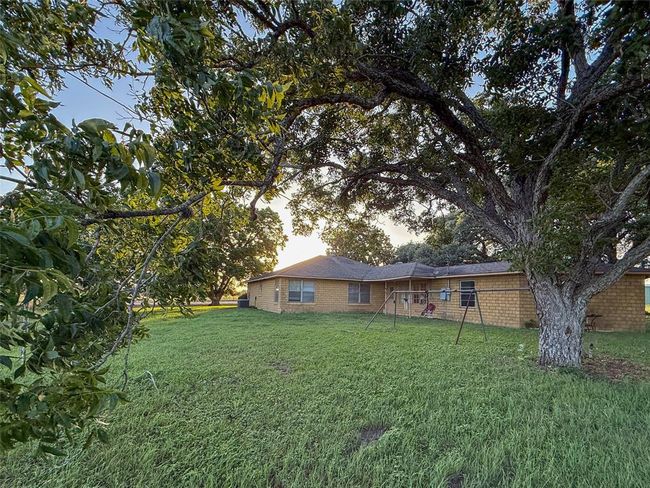 Charming single-story home with a cozy brick exterior, a small covered porch, and manicured bushes. Surrounded by lush greenery, it offers a serene and inviting atmosphere. | Image 20