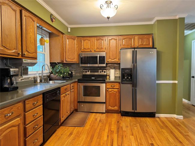 Kitchen featuring a sink, light wood-type flooring, crown molding, brown cabinetry, and stainless steel appliances | Image 9