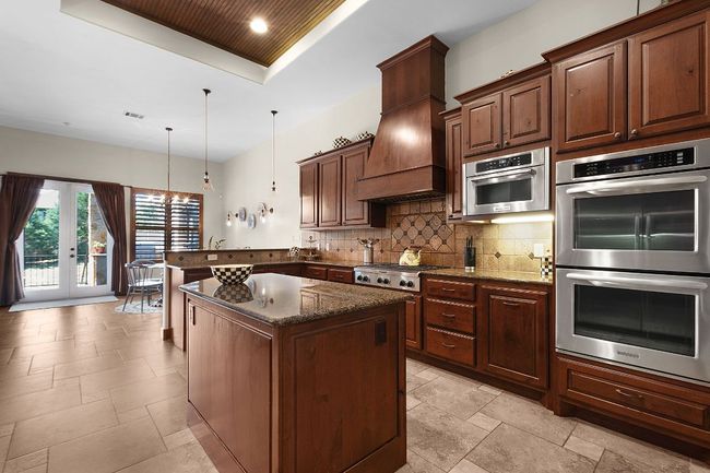 Kitchen with stainless steel appliances, an island, decorative backsplash, a chandelier, and granite counters | Image 9