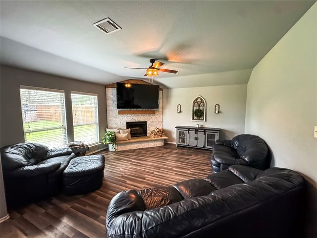 Living room with ceiling fan, a stone fireplace, visible vents, wood finished floors, and baseboards | Image 9
