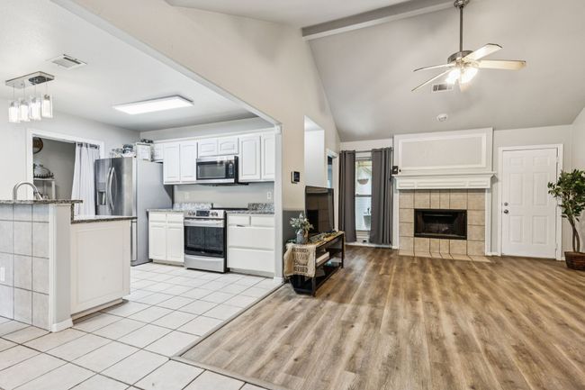 Kitchen with appliances with stainless steel finishes, a ceiling fan, white cabinetry, light stone counters, and a tiled fireplace | Image 4