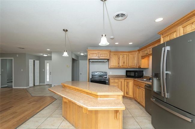 Kitchen with a center island, visible vents, black appliances, and light tile patterned floors | Image 13