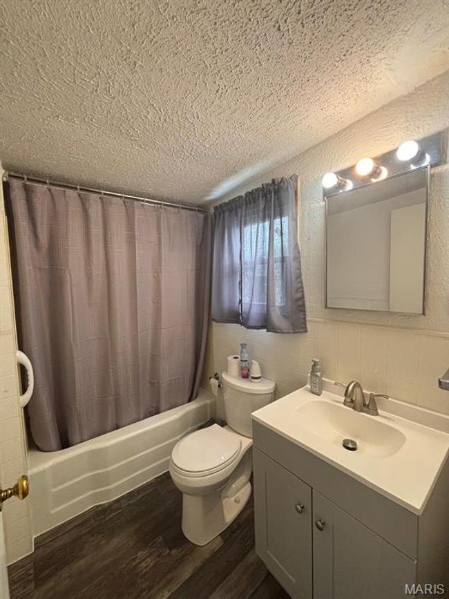 Bathroom with a textured ceiling, shower / bathtub combination with curtain, vanity, and wood finished floors | Image 21