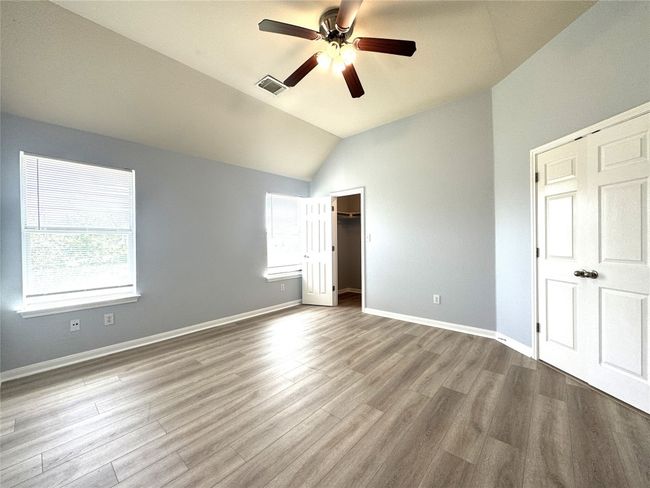 Unfurnished bedroom with vaulted ceiling, wood finished floors, a spacious closet, and ceiling fan | Image 8