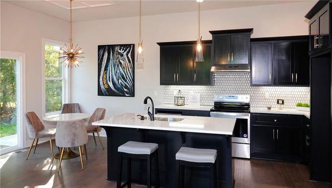 Kitchen featuring light countertops, stainless steel electric stove, tasteful backsplash, an island with sink, and decorative light fixtures | Image 17
