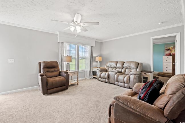 Living area featuring ceiling fan, a textured ceiling, carpet flooring, and ornamental molding | Image 5