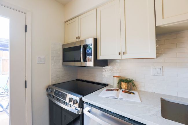 Kitchen with stainless steel appliances, tasteful backsplash, light stone quartz counters, and white cabinets. | Image 10