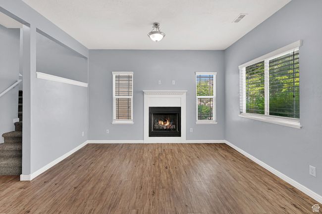 Unfurnished living room featuring stairway, wood finished floors, and a warm lit fireplace | Image 13