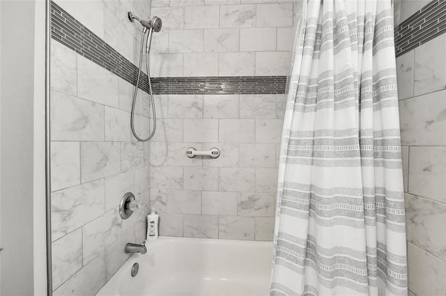 This bathroom features a clean, modern design shower. It includes a built-in bathtub with stylish striped shower curtain. | Image 16