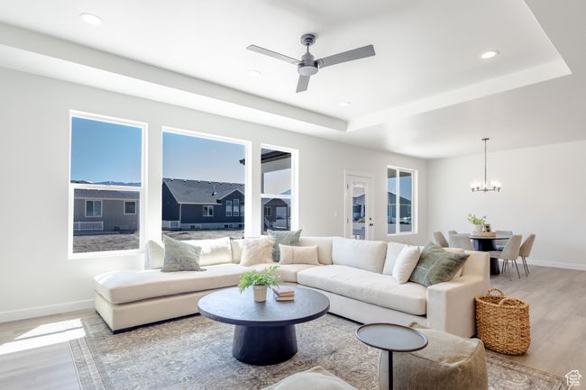 Living room with light wood-style floors, a chandelier, baseboards, a tray ceiling, and a ceiling fan | Image 9