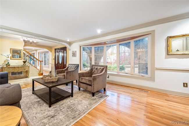 This 19.5' x 13' family room featuring a fireplace, detailed trim work, chair rail, and mirrored wall—anchored by hardwood floors and a wide architectural bay window. | Image 9