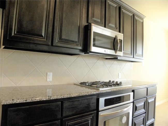 Kitchen featuring appliances with stainless steel finishes, tasteful backsplash, light stone countertops, and dark cabinetry | Image 12