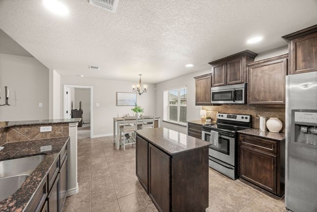 Kitchen featuring appliances with stainless steel finishes, a chandelier, tasteful backsplash, dark brown cabinets, and dark stone countertops | Image 14