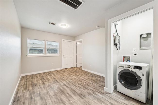 This photo shows a bright, compact laundry room with light wood flooring, neutral walls, and recessed lighting. It features a front-loading washing machine and a small window, adding natural light to the space. | Image 14