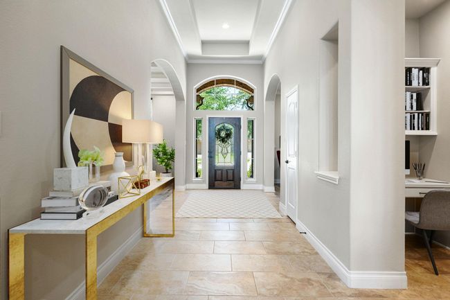 Step into elegance through this stunning entryway featuring soaring ceilings, tray detailing, and abundant natural light streaming through the decorative glass front door. The spacious foyer is anchored by sleek tile flooring adorned with modern decor. A built-in office nook adds functionality, while arched doorways lead seamlessly into the heart of the home. | Image 11