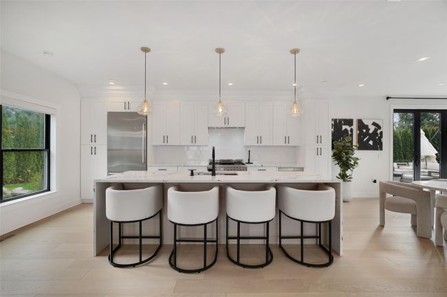 Kitchen featuring white cabinets, an island with sink, high quality fridge, backsplash, and baseboards | Image 4
