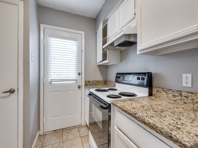Kitchen with electric range oven, under cabinet range hood, white cabinets, and light stone countertops | Image 7
