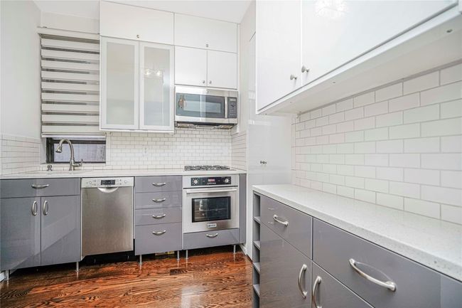Kitchen featuring stainless steel appliances, gray cabinetry, decorative backsplash, glass insert cabinets, and dark wood finished floors | Image 10