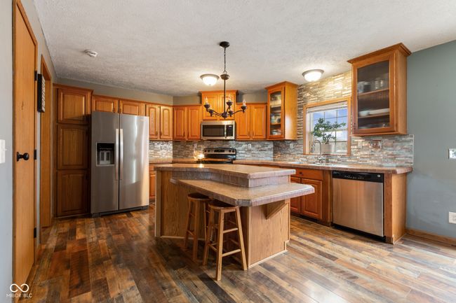 kitchen with brown cabinets, dark wood-type flooring, a chandelier, and stainless steel appliances | Image 6