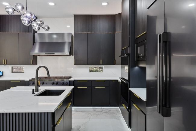 Kitchen with black appliances, wall chimney exhaust hood, recessed lighting, light stone countertops, and a sink | Image 12