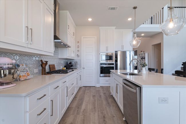 Kitchen featuring appliances with stainless steel finishes, a sink, wall chimney exhaust hood, backsplash, and light wood-style floors | Image 10